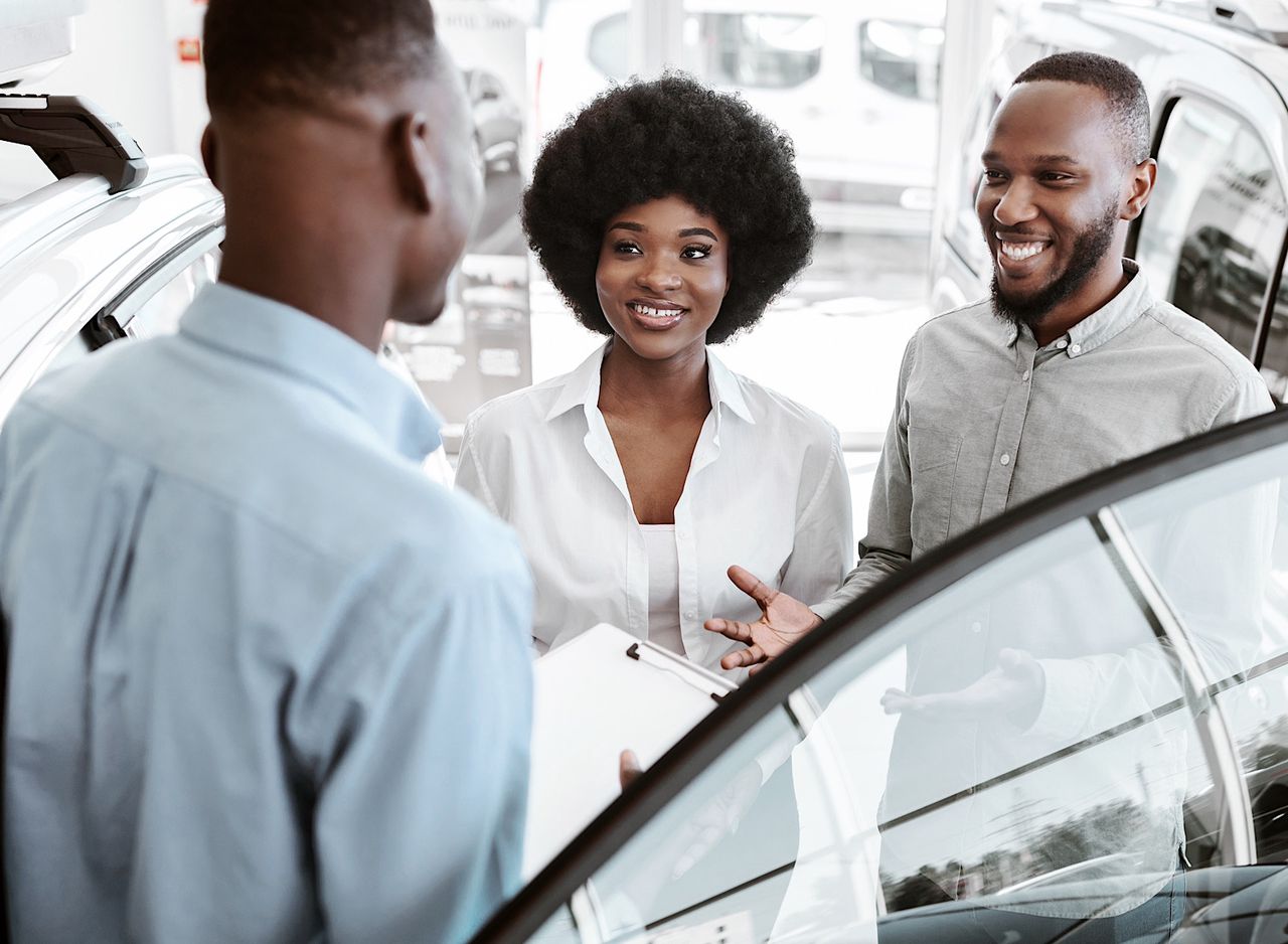 Young black couple selecting new car at auto dealership, salesman helping them make choice by Prostock-studio