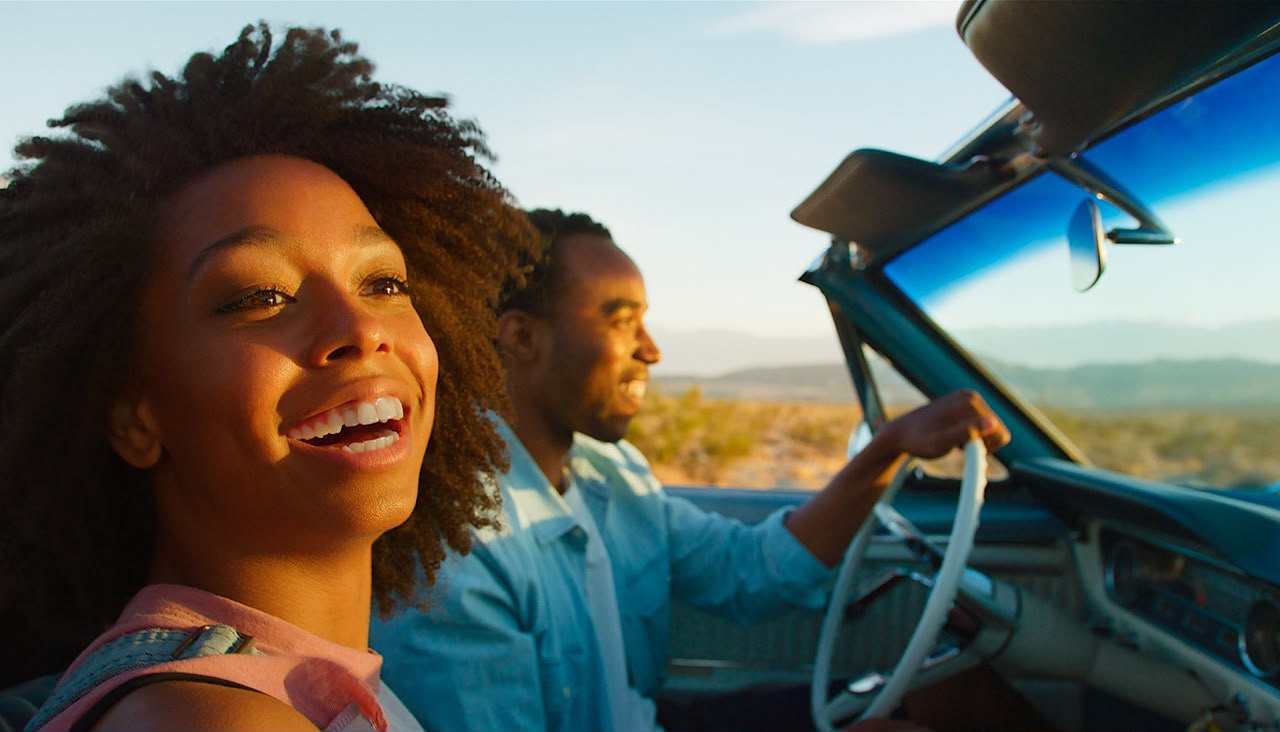 Close Up Of Couple Driving Classic Open Top Car On Road Trip Through Countryside At Sunset by monkeybusiness